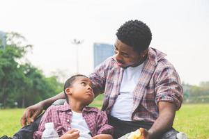 afrikanisch-amerikanischer vater und sohn beim picknick im park, glücksfamilienkonzepte foto