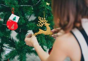 Rückansicht der Frau, die den Weihnachtsbaum zu Hause dekoriert und arrangiert und sich auf die Winterferien vorbereitet foto