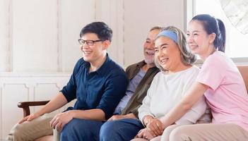 fröhliche asiatische familie, die im wohnzimmer fernsieht, senior vater mutter und sohn und tochter mittleren alters sitzen auf dem sofa, glücksfamilienkonzepte foto