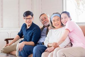 fröhliche asiatische familie im wohnzimmer, senior vater mutter und sohn und tochter mittleren alters sitzen auf dem sofa und blicken in die kamera, glücksfamilienkonzepte foto