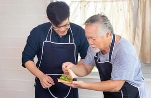 fröhlicher älterer asiatischer vater und sohn mittleren alters, die zusammen in der küche kochen foto