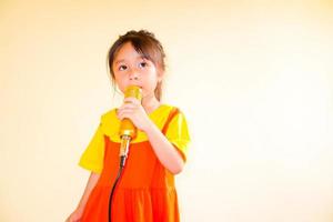 schönes baby trägt ein gelb-orangees outfit, gokowa-outfit oder mugunghwa, und hält goldenes mikrofon, das musik singt. Modekleid für Mädchen und Teenager. foto