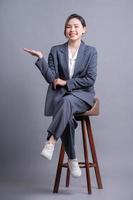 Junge asiatische Geschäftsfrau sitzt auf Stuhl und posiert auf grauem Hintergrund foto