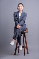 Junge asiatische Geschäftsfrau sitzt auf Stuhl und posiert auf grauem Hintergrund foto
