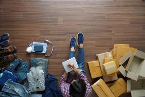 Draufsicht auf Frauen schreiben ein Notizbuch von zu Hause aus auf Holzboden mit Postpaket und verkaufen Online-Ideen-Konzept foto
