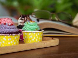 bunt von hausgemachtem Cupcake auf Holztablett und offenes Buch auf Holztisch. Konzept von Lifestyle und Entspannung. foto