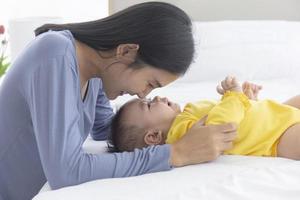 Eine asiatische Mutter spielt liebevoll und fürsorglich mit ihrem Baby im Bett. foto