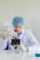 junger wissenschaftler, der mikroskop im labor verwendet. männlicher forscher mit weißem kittel, der am schreibtisch sitzt und proben mit dem mikroskop im labor betrachtet. wissenschaftler bei der arbeit im labor foto