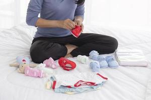 Eine asiatische Mutter saß im Bett und bereitete die Kleidung ihres Babys vor. foto