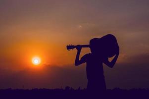 Die Silhouette eines Gitarristen, der eine Gitarre hält und ein Sonnenuntergang-Silhouette-Konzept hat. foto