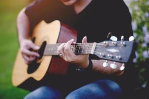 Bild eines Gitarristen, eines jungen Mannes, der Gitarre spielt, während er in einem natürlichen Garten sitzt, Musikkonzept foto