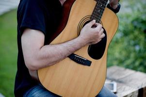 Bild eines Gitarristen, eines jungen Mannes, der Gitarre spielt, während er in einem natürlichen Garten sitzt, Musikkonzept foto