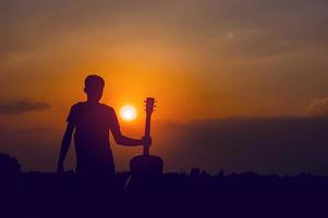 Die Silhouette eines Gitarristen, der eine Gitarre hält und ein Sonnenuntergang-Silhouette-Konzept hat. foto
