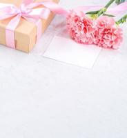 mai muttertag handgefertigtes geschenkbox-ideenkonzept, schöne blühende nelken mit babyrosa schleifengeschenk einzeln auf modernem marmorschreibtisch, nahaufnahme, kopierraum, mock up foto