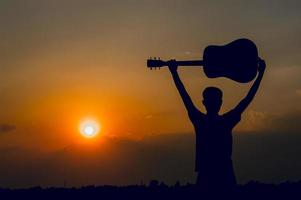 Die Silhouette eines Gitarristen, der eine Gitarre hält und ein Sonnenuntergang-Silhouette-Konzept hat. foto