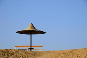 Sonnenschirm aus Stroh und Bank am Strand foto