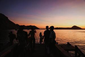 schwarze silhouette von touristen, die sich versammeln und fotoshootings mit meer und hügeln in labuan bajo machen foto