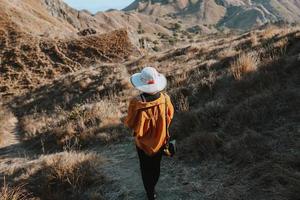 weibliche touristin mit sommerhut, die allein auf der insel padar den hügel hinuntergeht foto