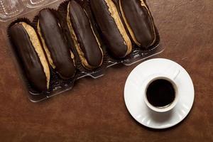 Schokoladen-Eclair auf einer weißen Untertasse und einer Tasse Kaffee foto