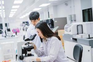 Zwei medizinische Wissenschaftler, die im medizinischen Labor arbeiten, junge Wissenschaftlerin, die sich das Mikroskop ansieht. Fokus auf junge Wissenschaftlerinnen wählen foto