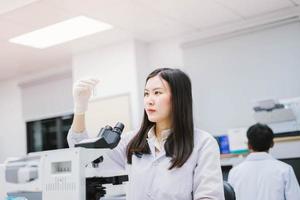 junge medizinische wissenschaftlerin, die reagenzglas im medizinischen labor betrachtet foto