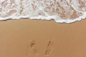 fußspuren im sand des strandes und weiße farbe der meereswellenblase foto