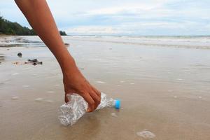 Hand der Frau pflückt eine leere Plastikflasche am Strand. foto