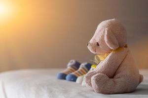 Der rosa kurzhaarige Teddybär sitzt in der Nähe der Schuhe des Neugeborenen auf einer weißen Matratze im Schlafzimmer, die das Baby auf die Geburt vorbereitet. werdende Mütter bereiten Neugeborenenzubehör und Teddybärspielzeug für ihre Babys vor. foto