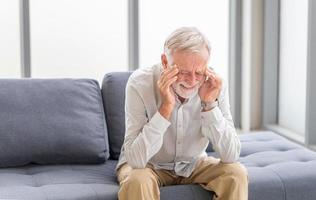 älterer mann, der kopfschmerzen hat und seinen kopf berührt, während er im wohnzimmer an einer migräne leidet, ein reifer mann drückt eine hand an den kopf und leidet unter unerträglichen schmerzen foto