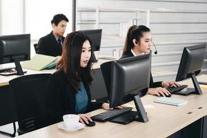 asiatische frau des jungen geschäftspersonals, die mit kopfhörern und computern zur unterstützung arbeitet. foto