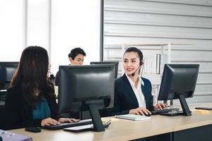 asiatische frau des jungen geschäftspersonals, die mit kopfhörern und computern zur unterstützung arbeitet. foto