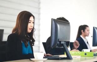 asiatische frau des jungen geschäftspersonals, die mit kopfhörern und computern zur unterstützung arbeitet. foto