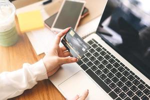 Hand der jungen erwachsenen Frau, die Kreditkarte für E-Commerce hält und Laptop-Computer verwendet. foto