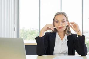 Schöne Geschäftsfrau in einem Anzug, ordentlich gekleidet in einem Bleistiftgriff, sitzt mit einem strahlenden Lächeln im Büro foto