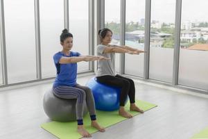 zwei asiatische frauen mittleren alters, die yoga machen, sitzen auf einem gummiball im fitnessstudio. foto