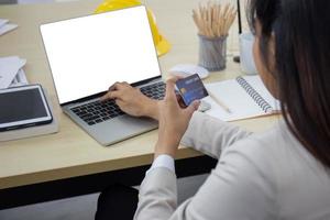 Eine junge professionelle asiatische Geschäftsfrau, die einen Laptop und eine Kreditkarte verwendet, um online zu bezahlen, während sie an ihrem Schreibtisch sitzt. foto
