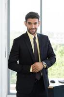 Ein Geschäftsmann in einem ordentlich gekleideten Anzug, der mit einem strahlenden Lächeln im Büro steht foto