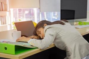 Eine junge asiatische Geschäftsfrau schläft auf ihrem Schreibtisch. foto