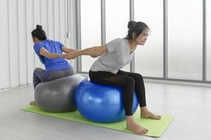 zwei asiatische frauen mittleren alters, die yoga machen, sitzen auf einem gummiball im fitnessstudio. foto