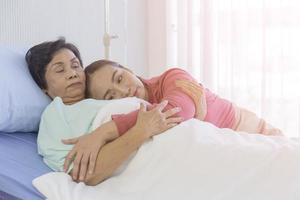 eine asiatische frau umarmt ihre mutter, die sich auf einem krankenhausbett erholt. foto