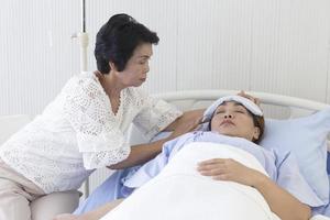 Eine asiatische Mutter kümmert sich in einem Krankenhausbett um ihre kranke Tochter. foto