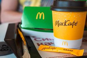 ein pappbecher mcdonald's kaffee mit der aufschrift maccafe auf russisch und ein hamburger in einer schachtel auf einem tablett. Fast-Food-Restaurantketten. Russland, Kaluga, 21. März 2022. foto