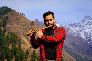 kleiner Junge, der Bansuri-Indianerflöte in den Bergen spielt foto