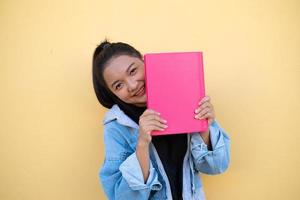 glückliches junges mädchen des studenten mit rosa buch auf braunem hintergrund. foto