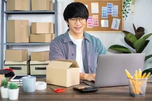 asiatischer mann unternehmer start kleinunternehmer sme freiberuflicher mann, der mit box arbeitet, um online-marketing-verpackungs- und lieferszene im büro zu hause, onlinebusiness-verkäuferkonzept.
