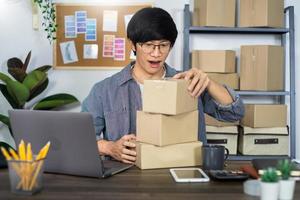 asiatischer mann unternehmer start kleinunternehmer sme freiberuflicher mann, der mit box arbeitet, um online-marketing-verpackungs- und lieferszene im büro zu hause, onlinebusiness-verkäuferkonzept.