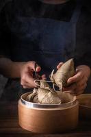 zongzi, frau, die gedünsteten reisknödel auf holztisch essen wird, berühmtes leckeres essen im drachenbootfestival duanwu-designkonzept, nahaufnahme, kopienraum foto