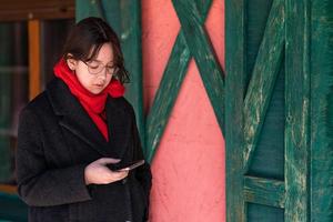 Ein Mädchen mit einem Telefon in der Hand steht auf der Straße in der Nähe eines rosafarbenen Hauses mit grünen Fensterläden foto