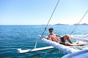asiatischer Mann mit Sonnenbrille, der sich auf dem Katamaran-Netz entspannt und die Sommerzeit genießt foto