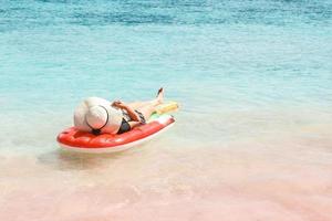 frau im sommerhut, die auf aufblasbarer wassermatratze am rosa sandstrand von labuan bajo liegt foto